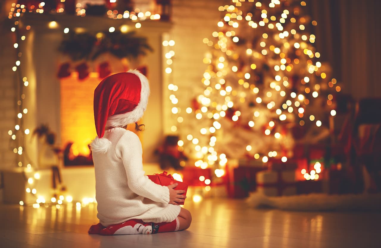 child girl sitting back in front of Christmas tree on Christmas Eve
