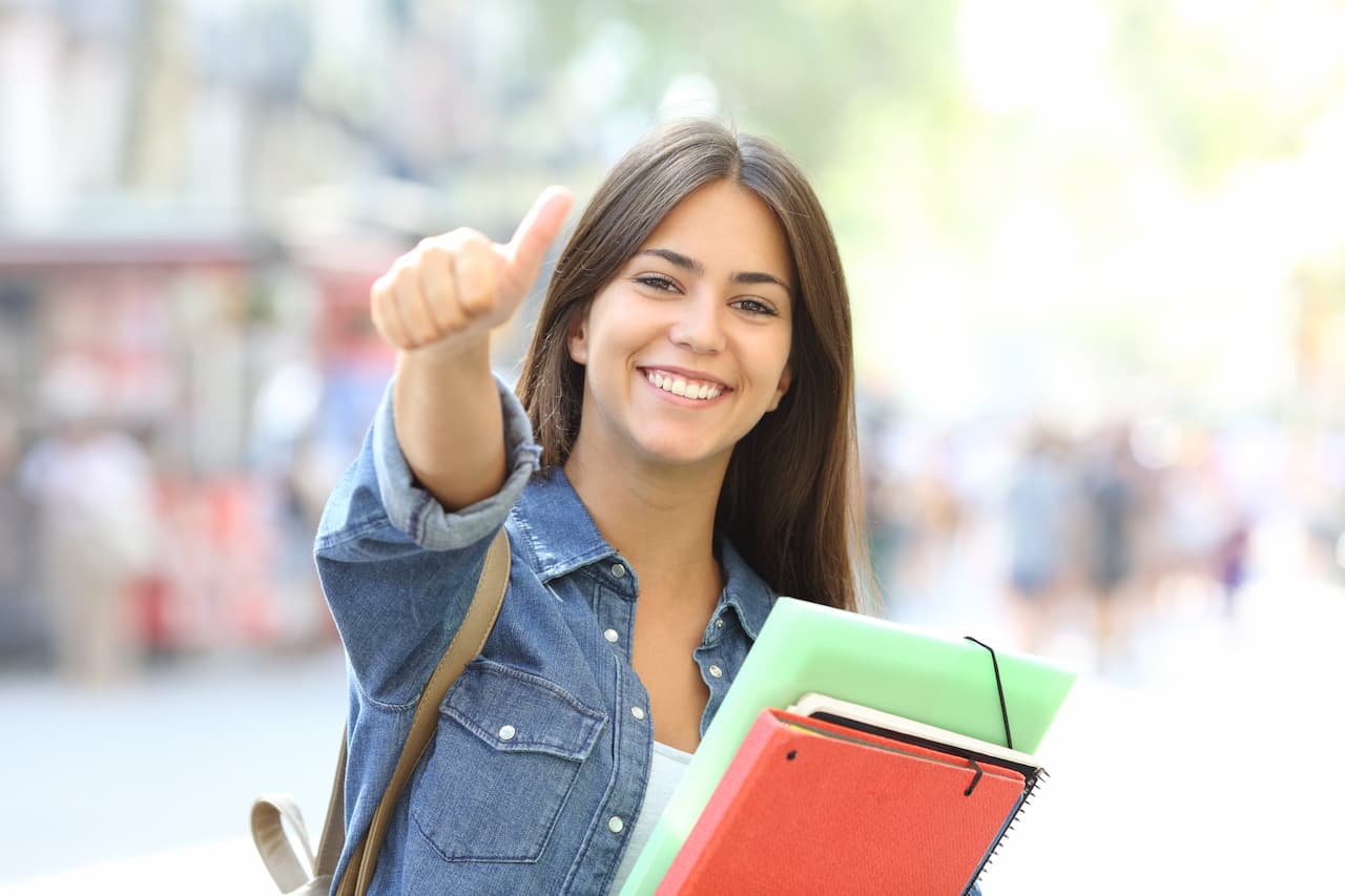 Happy student posing with thumbs up in the street